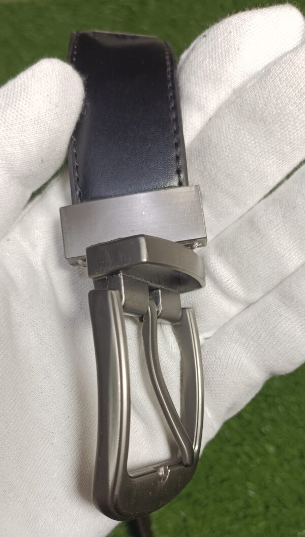 Close-up of a black leather belt featuring a silver metal buckle held in a gloved hand.